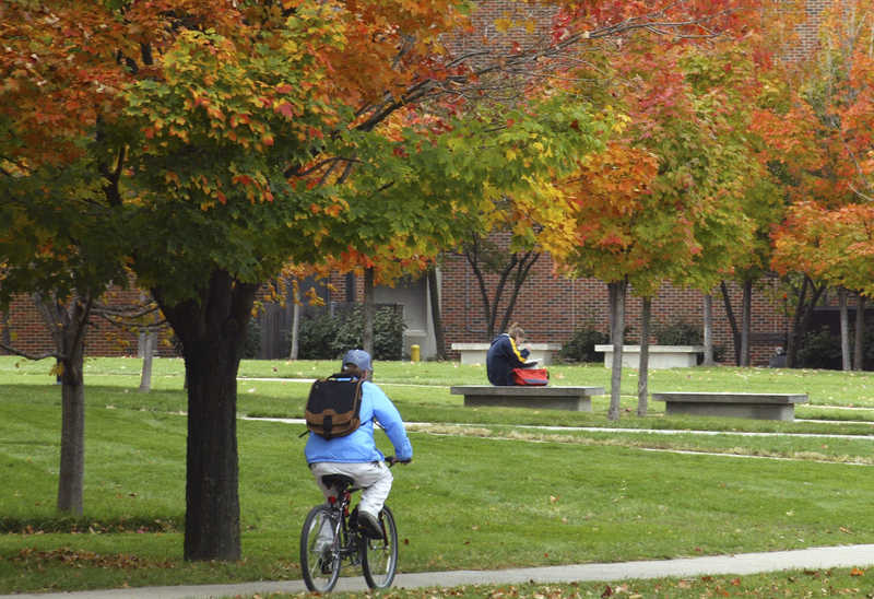 View of park, with a person riding a bike and another sitting, reading