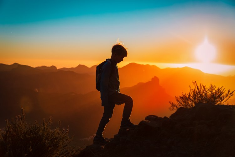 Silhouetted boy climbing mountain