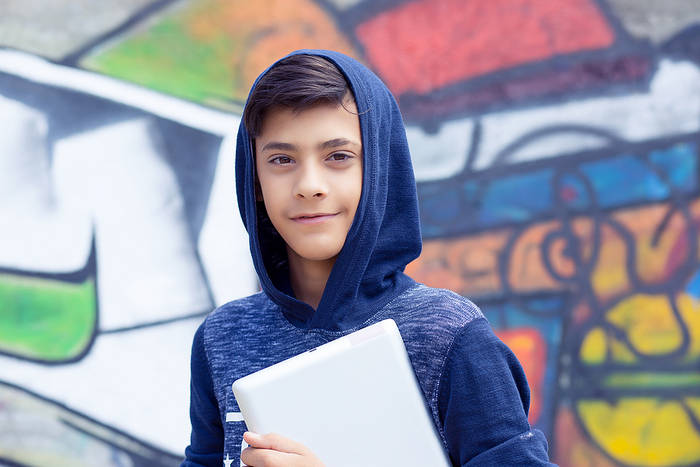 Boy in a blue hoody looking at the camera, holding a tablet computer