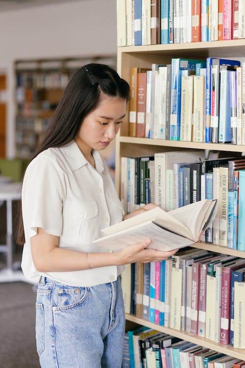 Girl standing looking through book in front of library shelves