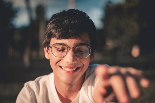 Head and shoulders shot of teenage boy wearing glasses and reaching towards camera