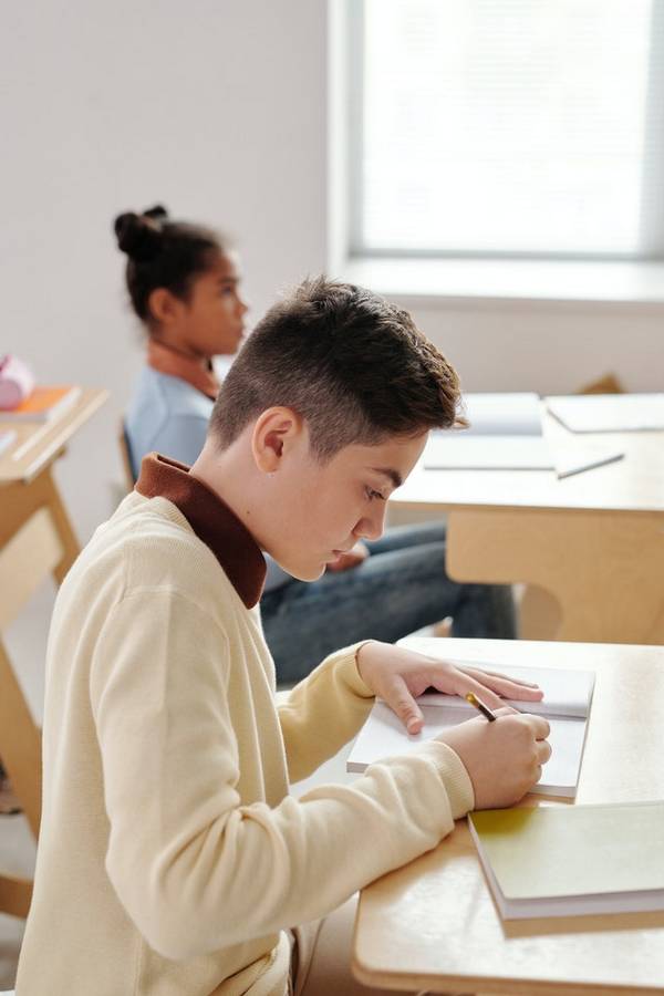 Side-on view of teenage boy sitting at desk writing