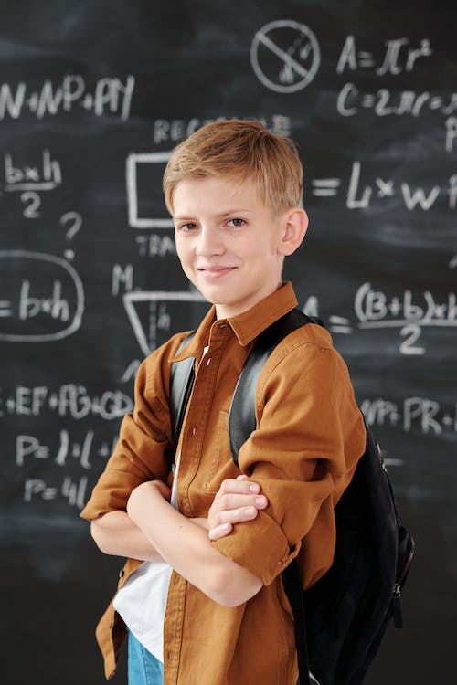 Boy standing with crossed arms in front of chalkboard