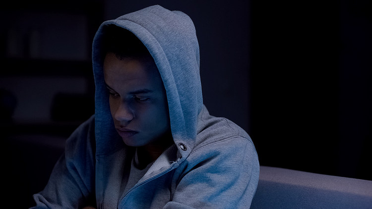 African-american teen boy sitting in dark room suffering depression, loneliness