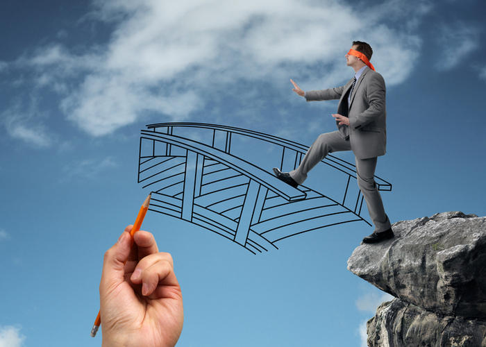 Blindfolded businessman stepping off cliff on to a bridge being drawn by a huge hand