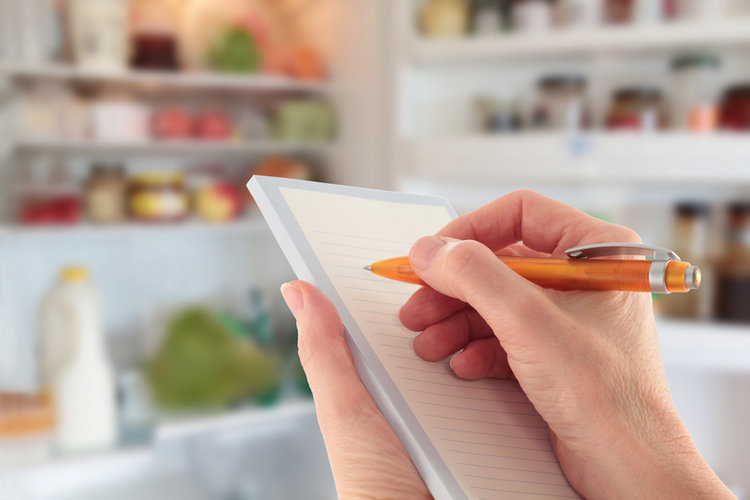 Hand writing list in front of open fridge