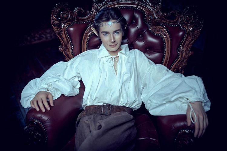 A smiling majestic prince of elves sitting in a vintage armchair in his magic castle