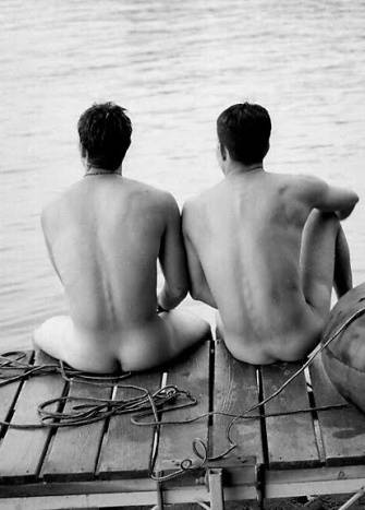 Rear view of two nude young men sitting on a dock