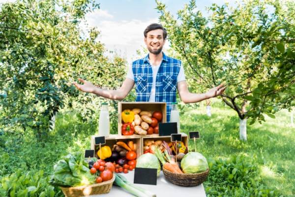 Young man standing behind display of fruit and vegetables