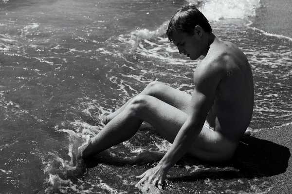 Naked young man sitting at the edge of the water