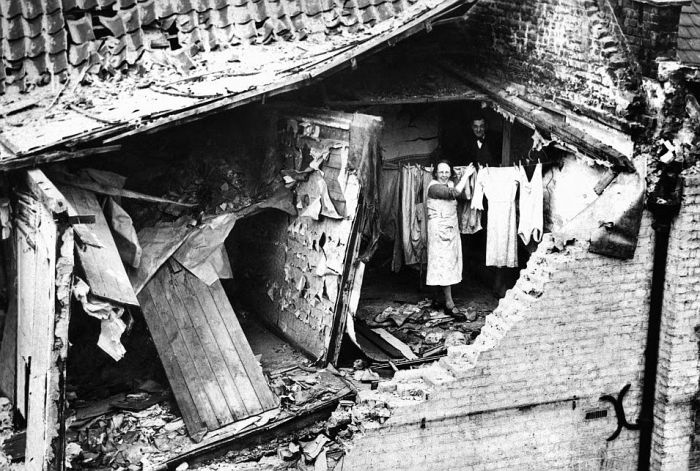 A smiling woman hanging out washing in a bomb-damaged house