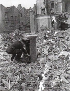 A post office worker emptying a postbox in an area strewn with rubble