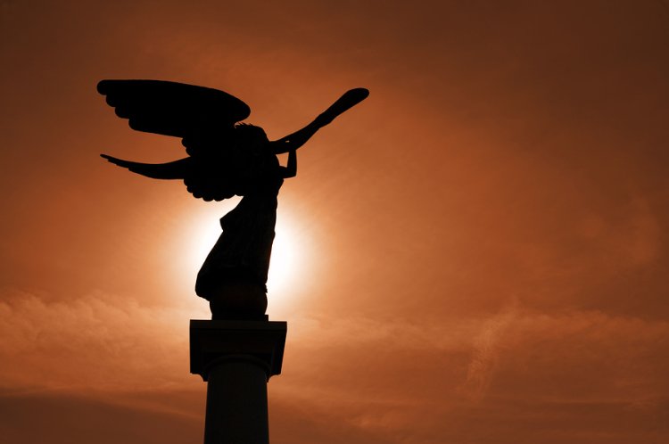 Silhouette of angel with cornet against sunset